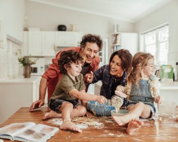 Joyful mother and father looking at young son and daughter in kitchen while mixing ingredients in a bowl