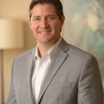 certified financial planner Marshall Clay wears a gray jacket and white shirt while posing for professional photo in office