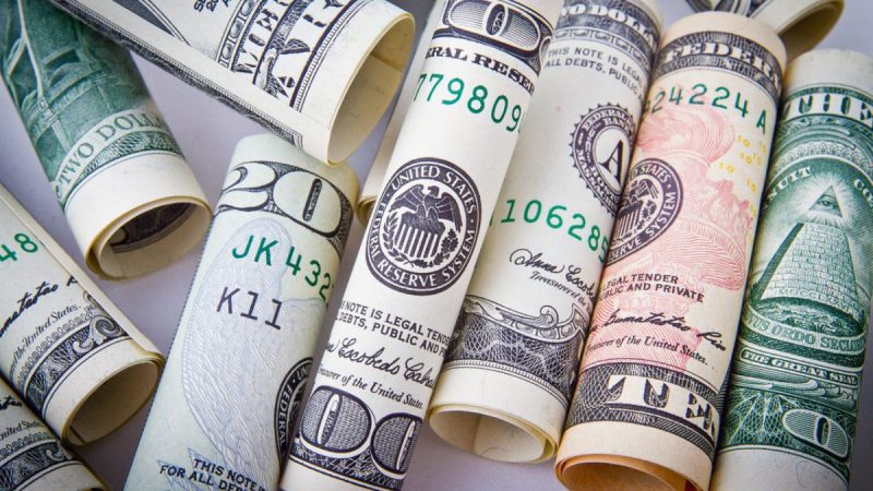 various US currency rolled tightly and lined up together, including a twenty and one hundred dollar bill